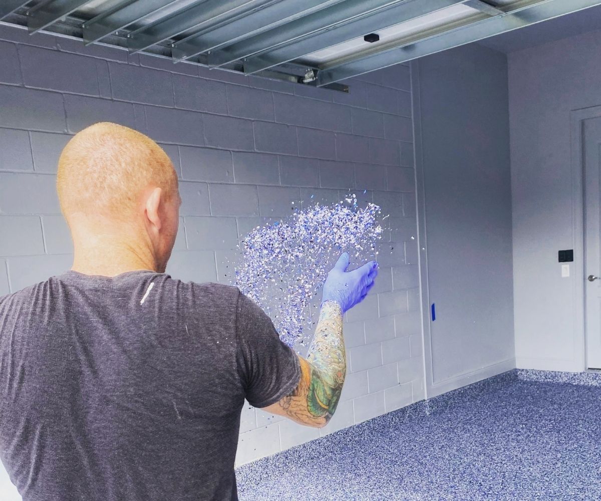 Broadcasting blue and white vinyl flake into a garage floor coating in Saint Augustine, Florida
