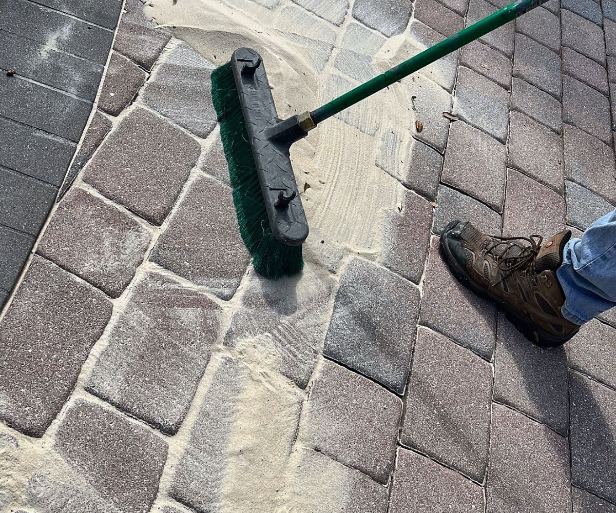 Sweeping polymeric sand into paver joints on a pool deck after a repair in Saint Augustine, Florida