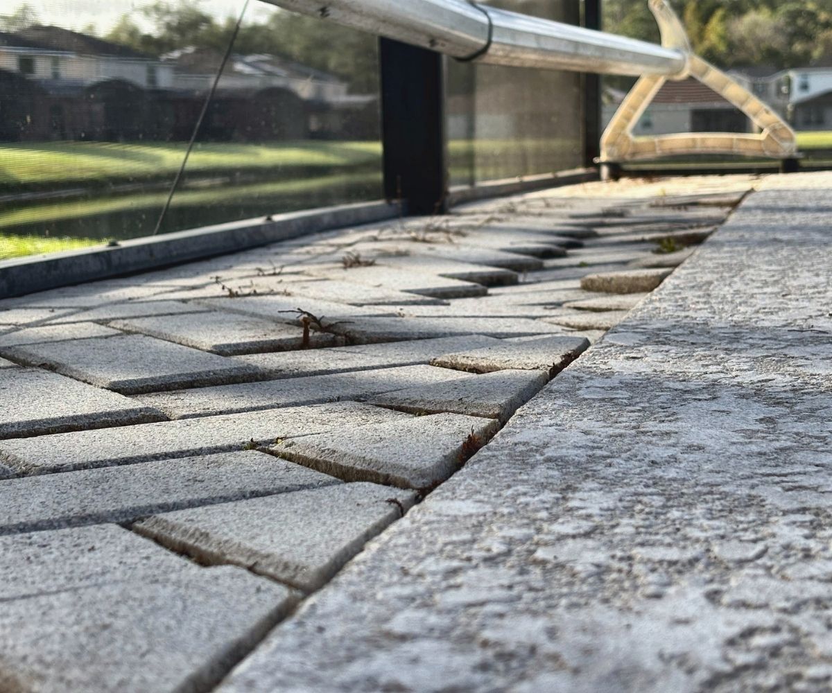 Sunken, uneven pavers with weed growth on a screened pool deck in Saint Augustine, Florida