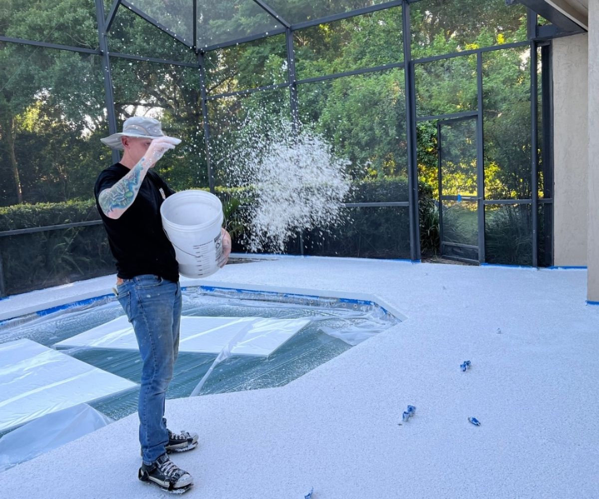 Broadcasting white flake into a concrete coating on a screened pool deck in Saint Augustine, Florida